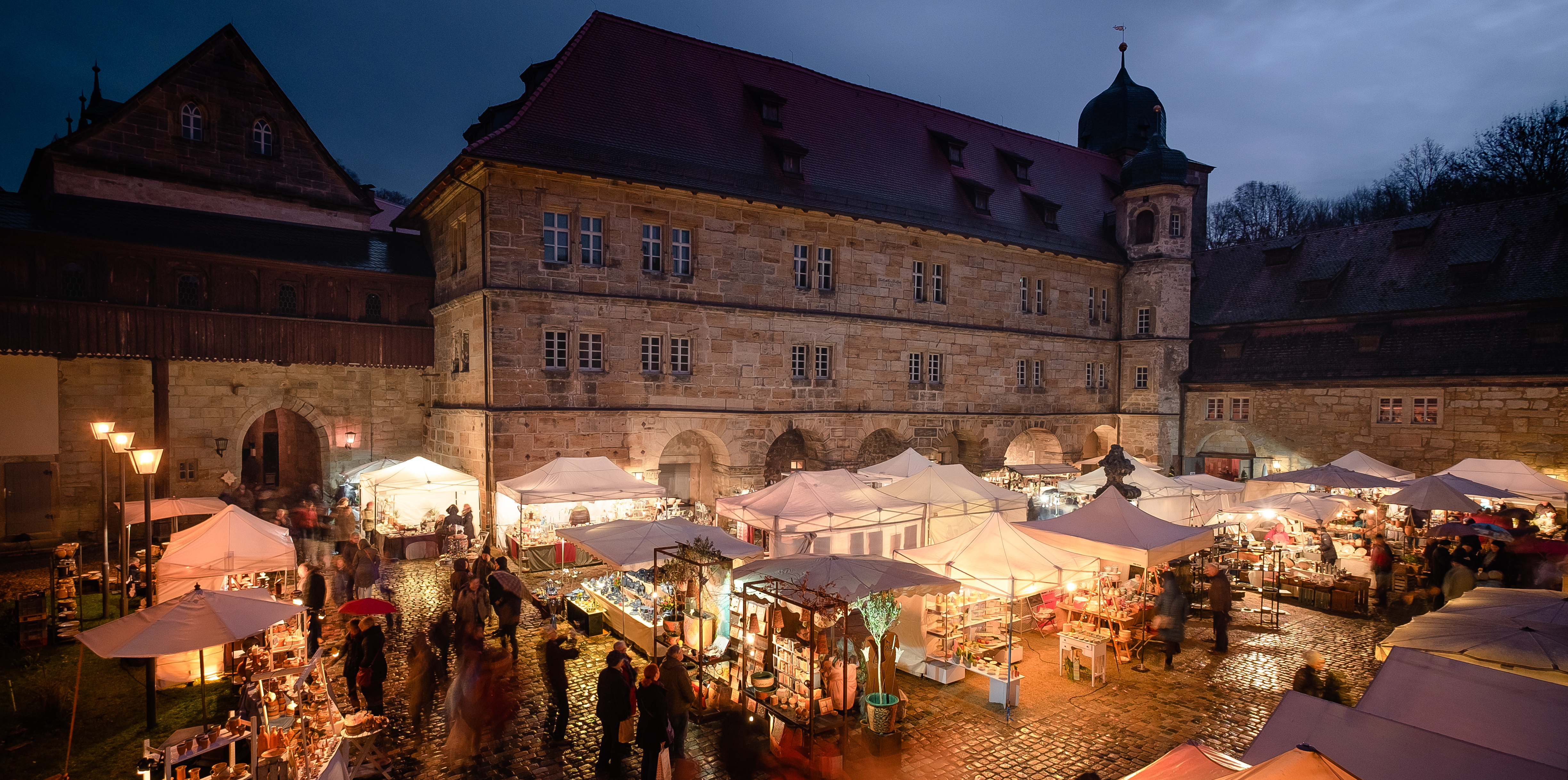 Innenhof des Schloss Thurnau mit hell erleuchteten Ständen des Töpfermarktes, dunkler Himmel im Hintergrund